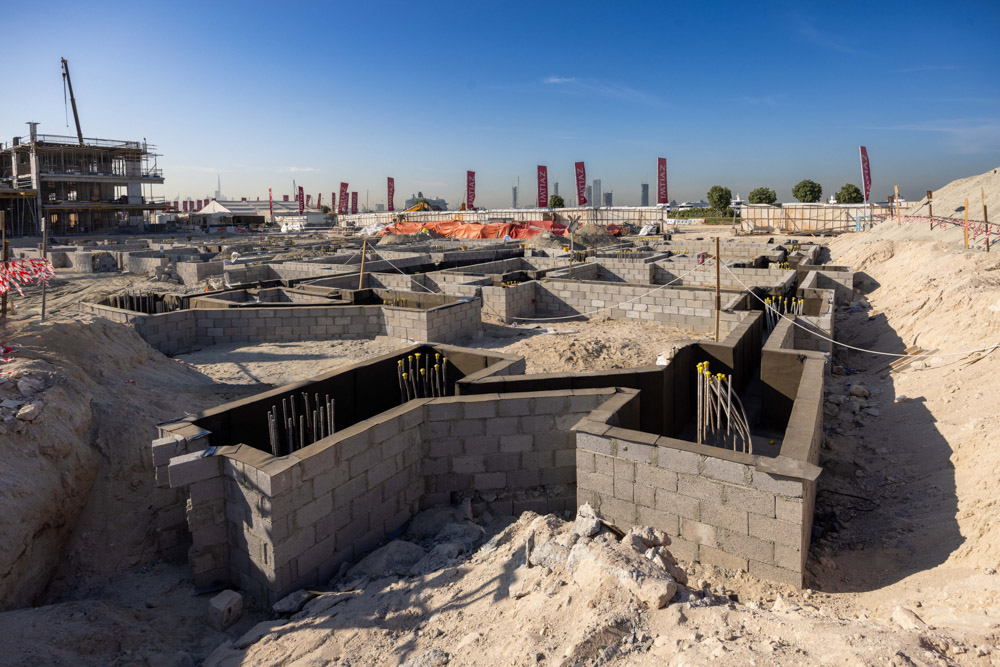 Cotier House 2 By Imtiaz Construction site with concrete block foundations and rebar, surrounded by excavation and clear blue sky.